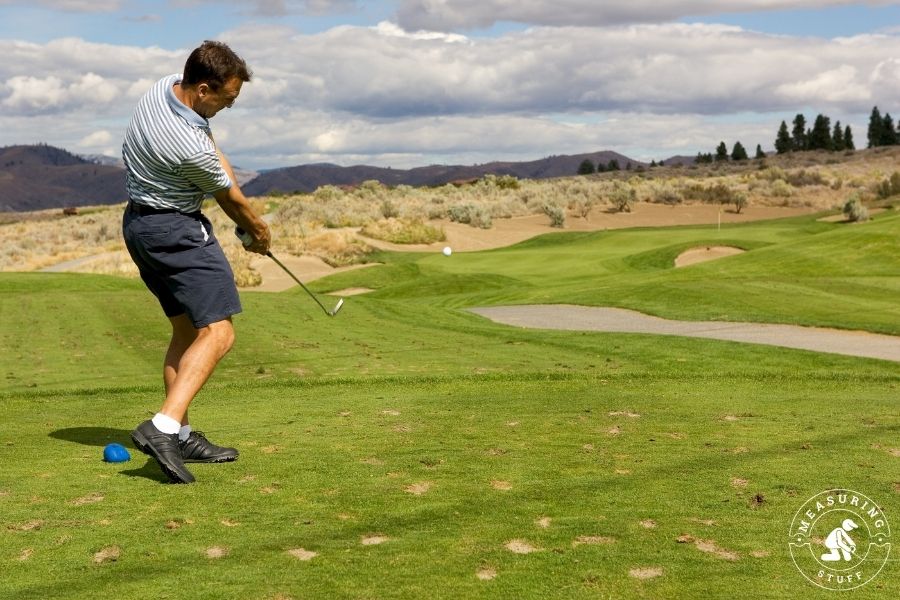 man swinging golf club from the rough fairway