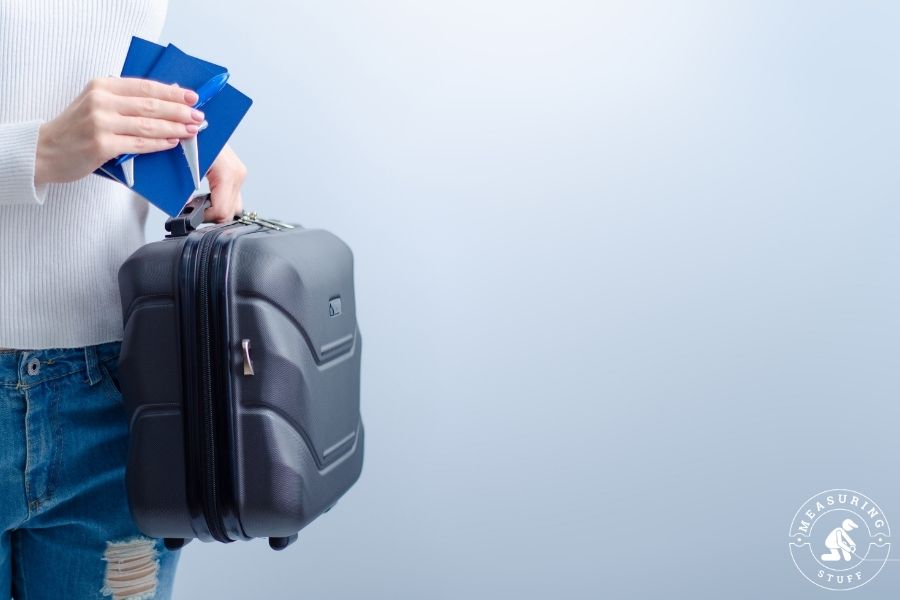 man holding grey suitcase and airline tickets