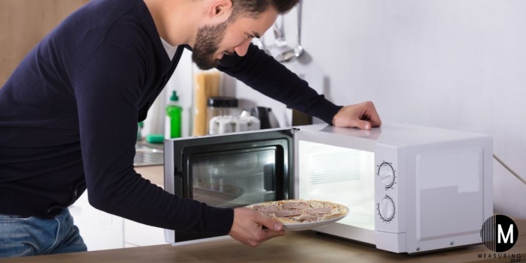 man putting dinner plate in microwave