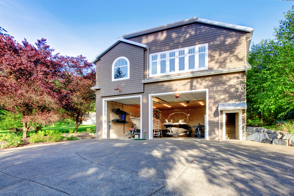 Luxury gray house with white trim and two motor boats in garage. Spacious driveway with concrete floor.