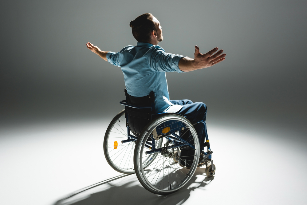 man sitting in a basic wheelchair with arms outreached