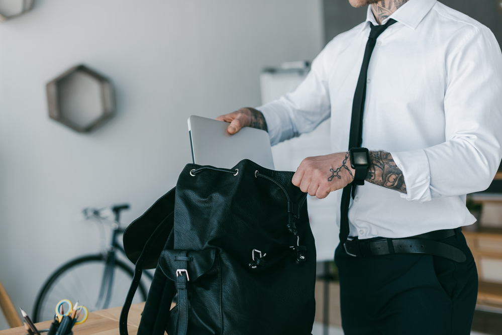man wearing shirt and tie placing laptop into a backpack