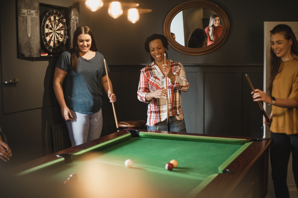 Small group of female friends playing a game of pool in a games room in a house.