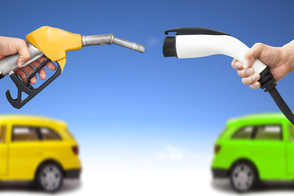 electric car and gasoline car concept. hand holding gas pump and power connector for refuel