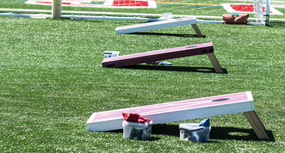 Three homeaide wooden corn hole game boards are set up side by side on a green turf field with bean bags in containers.