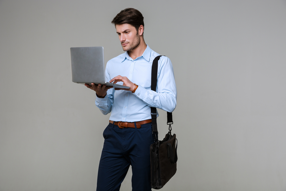 Image of caucasian businessman in office clothes holding laptop computer isolated over gray background