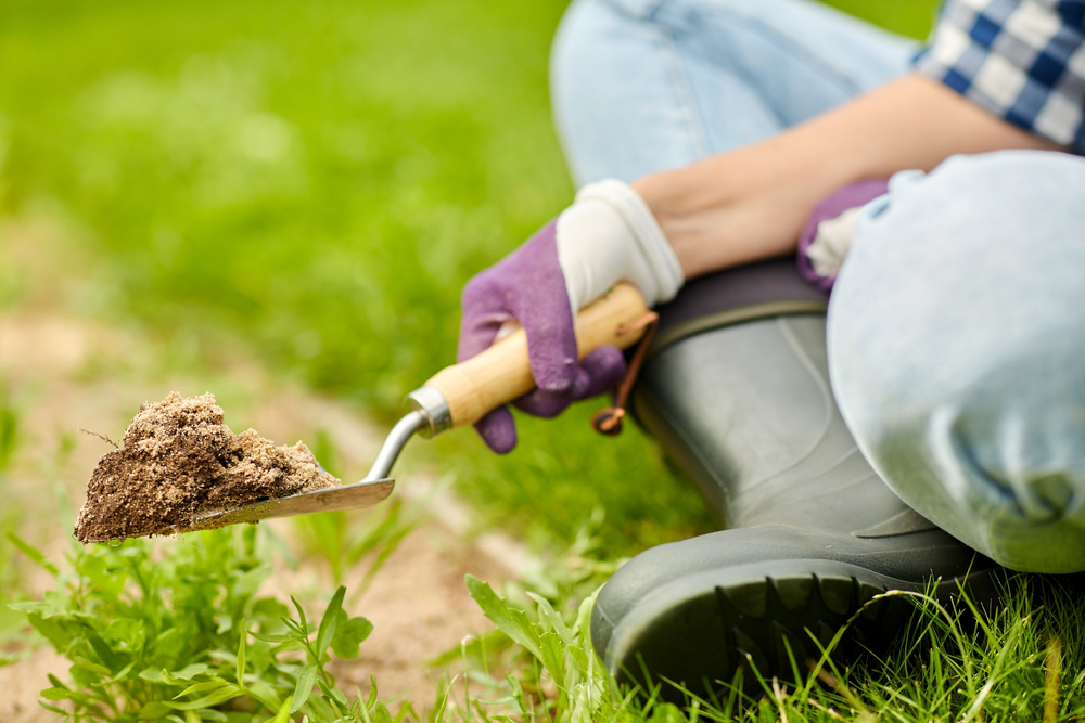 hand digging flowerbed ground with garden trowel