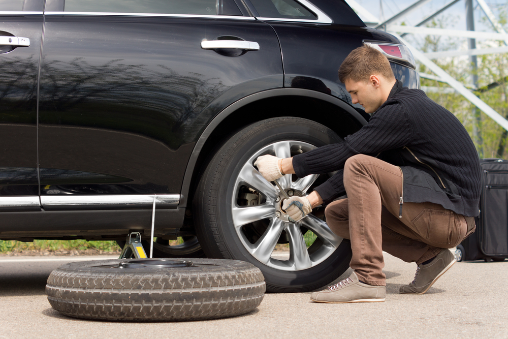 Young man changing the punctured tyre on his car loosening the nuts with a wheel spanner before jacking up the vehicle