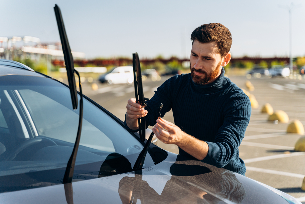 Man is changing windscreen wipers on a car while standing at the street