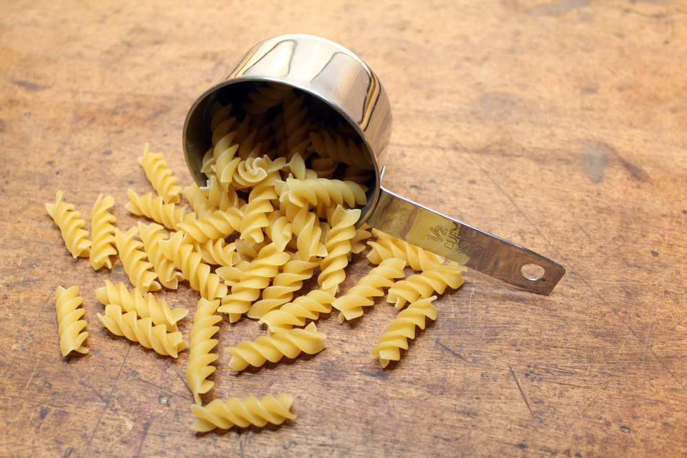 Measuring cup fill of spiral pasta over wood background