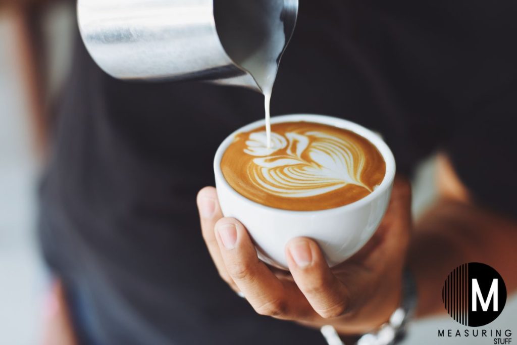 pouring cream into a coffee mug forming a flower pattern