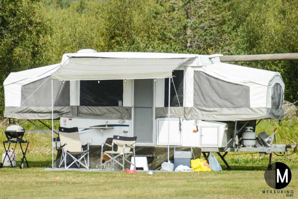 extended pop up camper in an open field with chairs and bbq