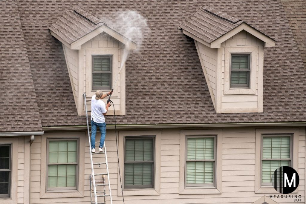 man pressure washing a house on a ladder