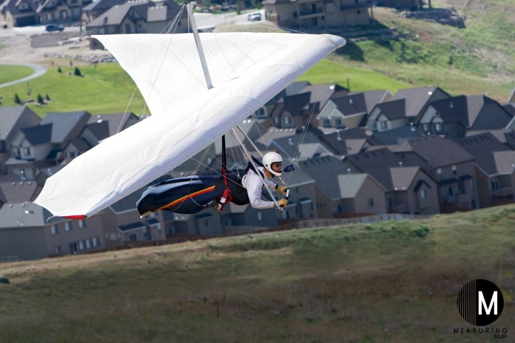 man hang gliding on a hill with houses in the background