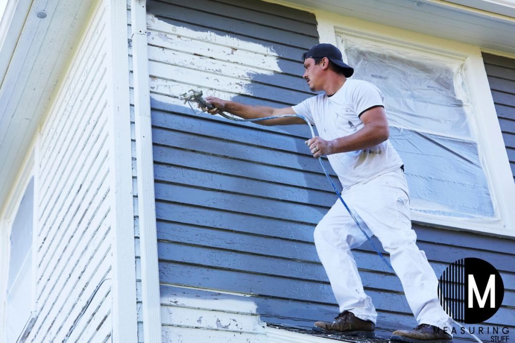 man spray painting the house exterior