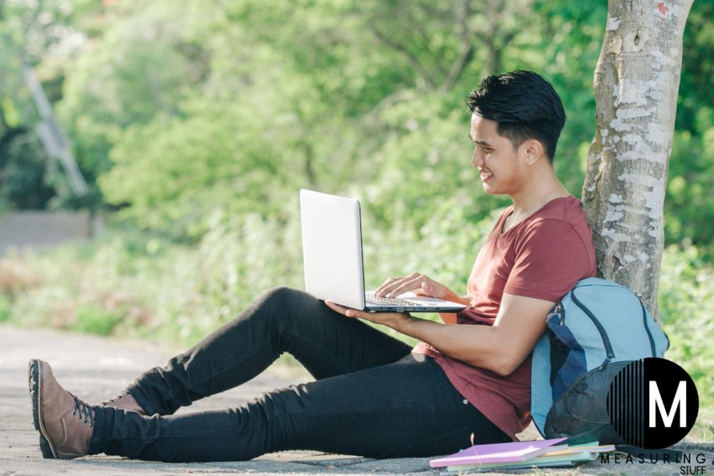 man using a laptop sitting beside a tree