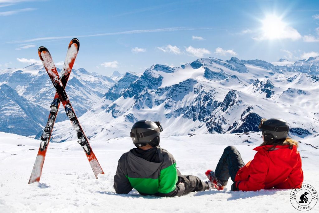 A couple sitting in the snow with vertical skis