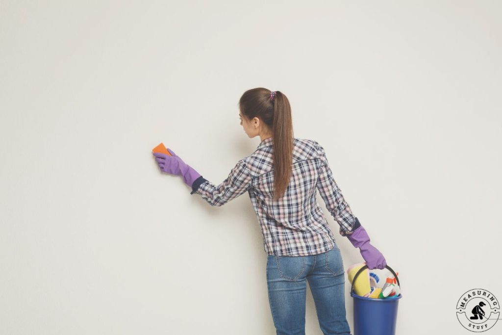 woman washing a wall with a sponge and cleaners