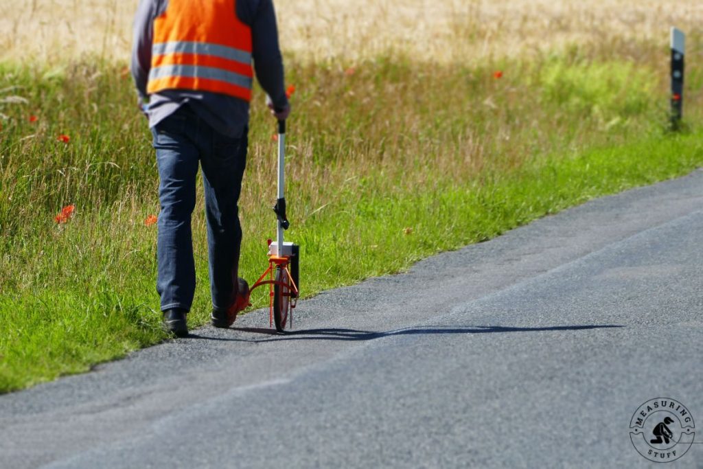 worker rolling a measuring wheel along paved road