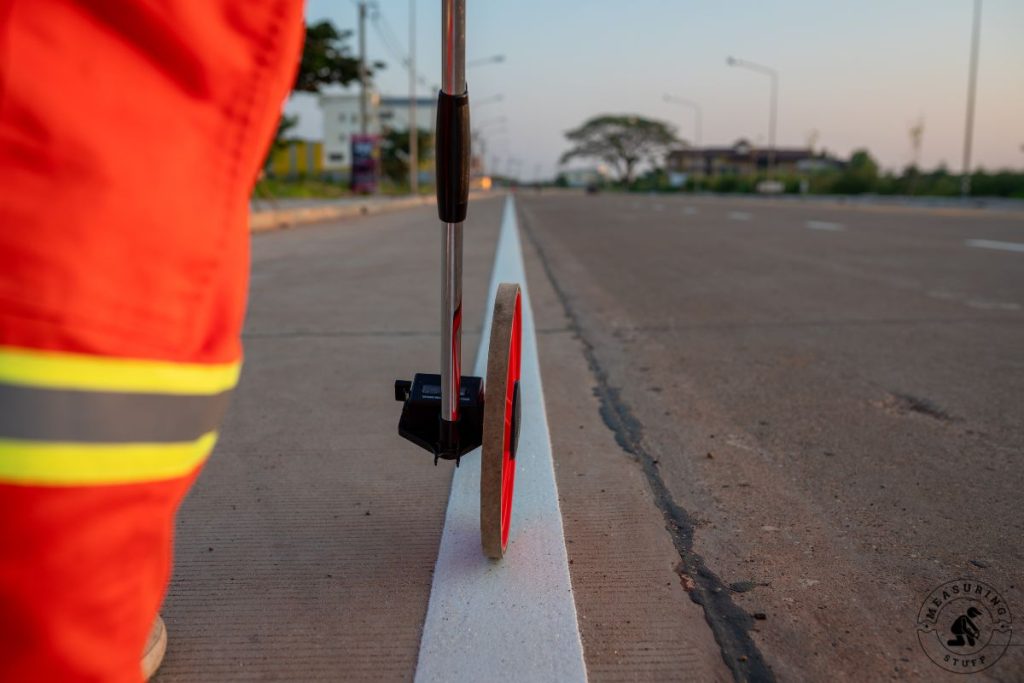 construction worker using a measuring wheel on a white line
