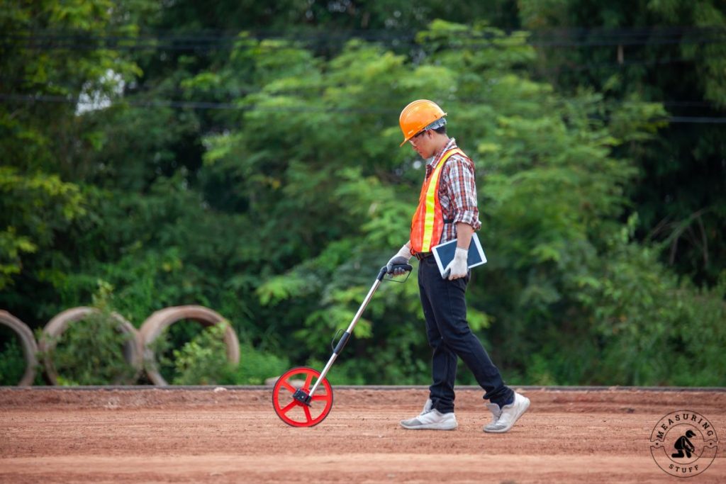 worker using a measuring wheel in a dirt field