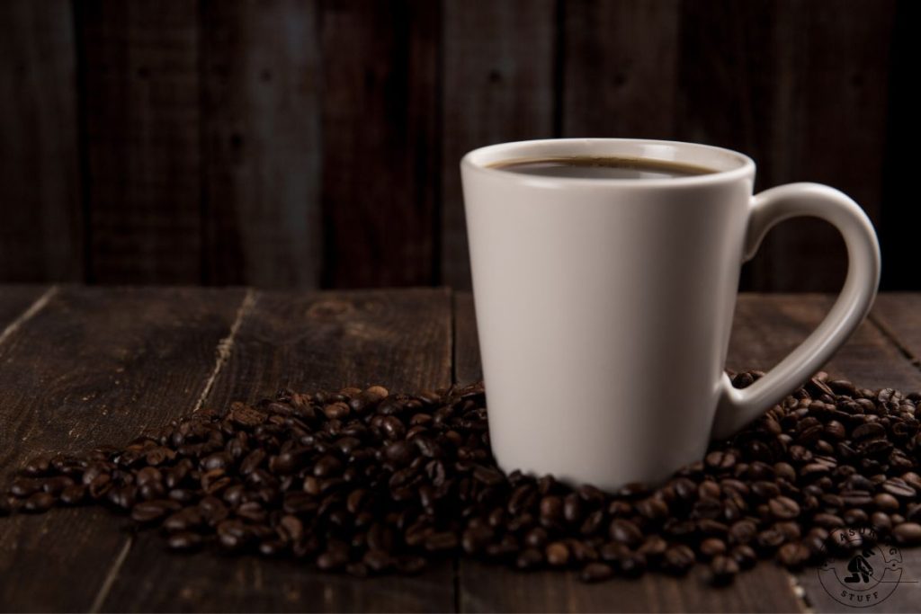 white ceramic mug filled with coffee surrounded by coffee beans