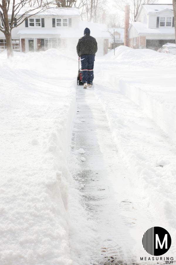 man using a snowblower on a long driveway