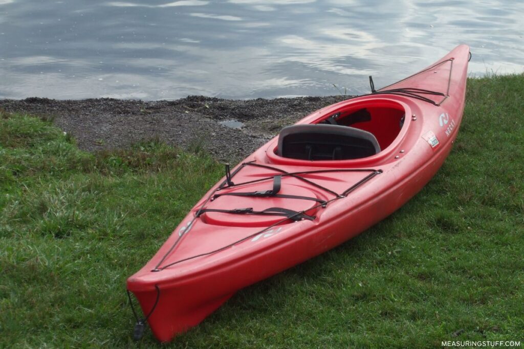 empty red kayak sitting on grass next to water