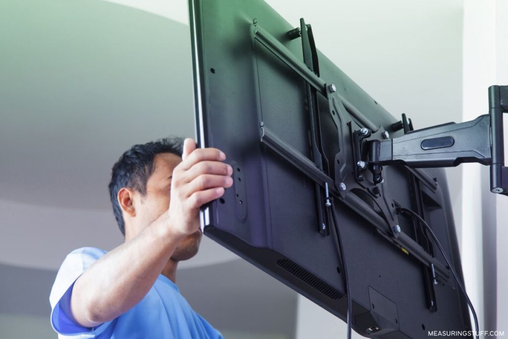 man placing a tv on wall 