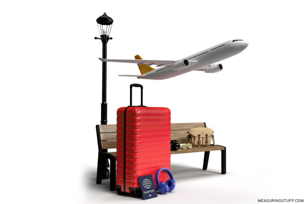 hardshell luggage next to a bench, light pole, and airplane overhead