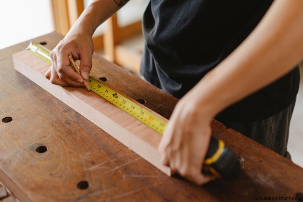 carpenter using a measuring tape on a piece of lumber