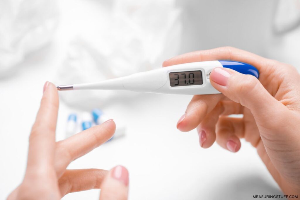 holding a digital thermometer reading 37.0 celcius
