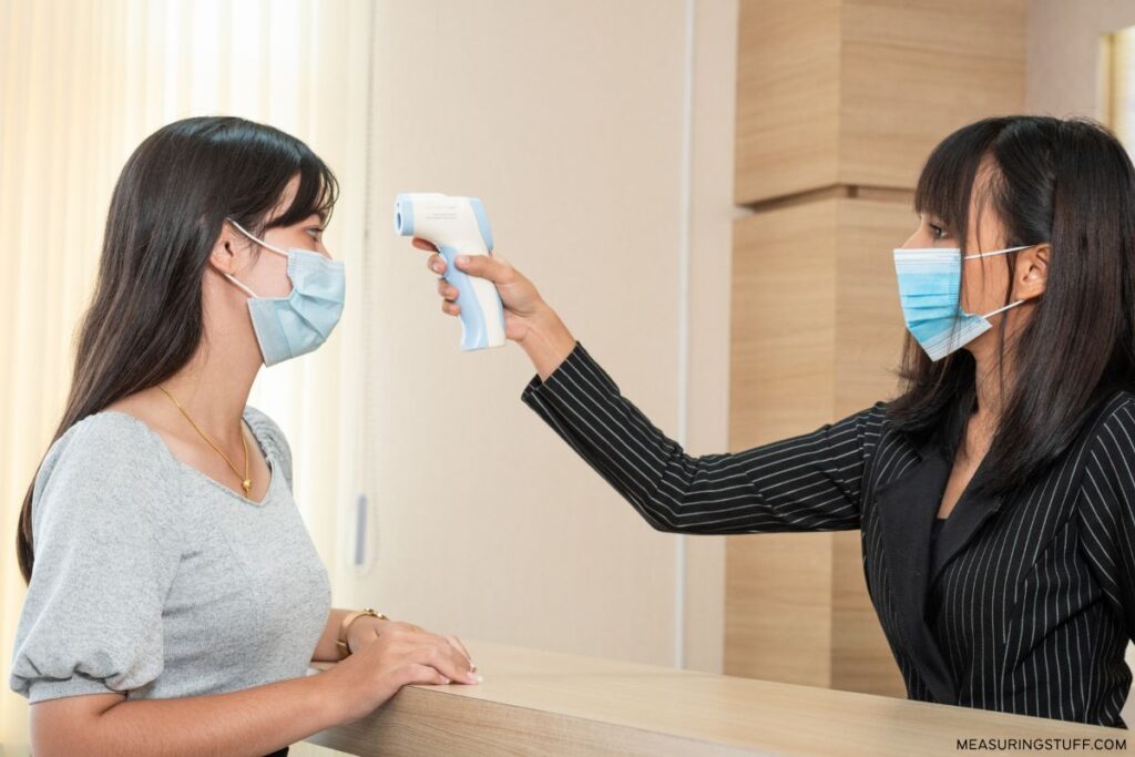 woman wearing a mask using infrared thermometer to check temperature of a woman wearing a mask