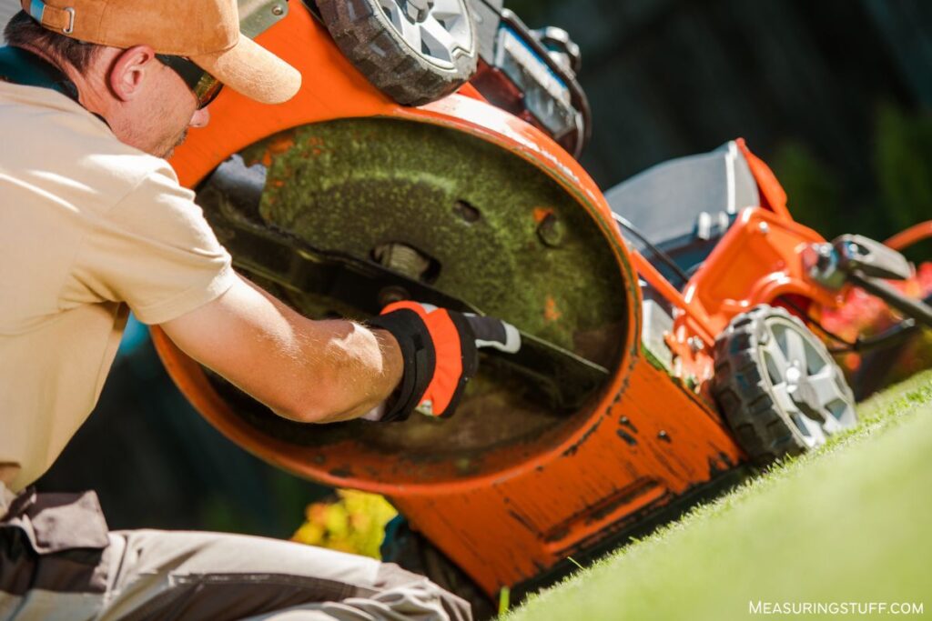 man cleaning grass from lawn mower blades